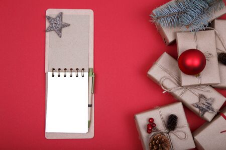 Christmas composition. Christmas gift, notebook, pine cones, fir branches on red background. Flat lay, top view, copy spaceの写真素材