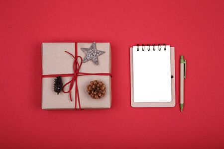 Christmas composition. Christmas gift, notebook, pine cones, wooden star on red background. Flat lay, top view, copy spaceの写真素材