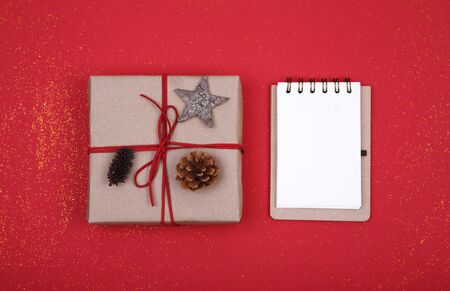 Christmas composition. Christmas gift, notebook, pine cones, wooden star on red background. Flat lay, top view, copy spaceの写真素材