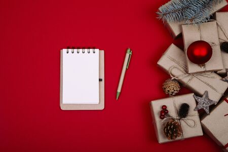 Christmas composition. Christmas gift, pine cones, fir branches, notebook on red background. Flat lay, top view, copy spaceの写真素材