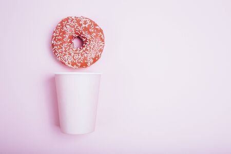 Donuts with icing and paper cup on pastel pink background. Sweet donuts.の写真素材