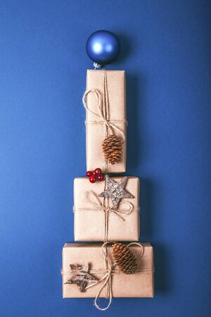 Christmas gift boxes with decoration laid out in the shape of a Christmas tree on blue background, overhead view.の写真素材