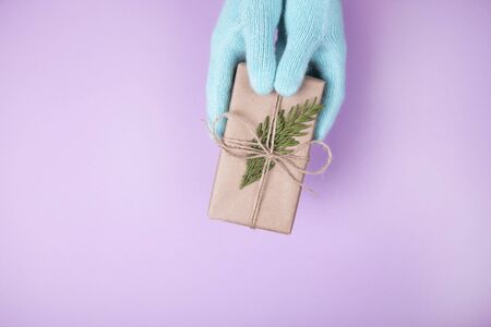 Woman's hands in blue gloves holding craft paper gift box with a present for Christmas, new year, valentine day or anniversary on pink background, top viewの写真素材
