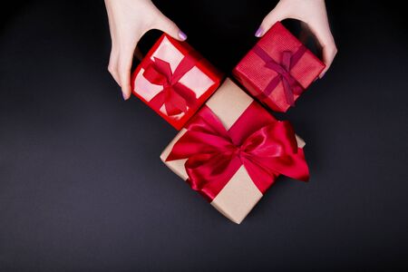 Woman's hands holding craft paper gift boxes with a presents for Christmas, new year, valentine day or anniversary on black background, top viewの写真素材