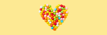 Old fashion pale multi colored candy heart background on yellow. Banner
