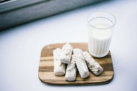 Glass of fresh milk and white chocolate cookies on wooden board over white backgroundの写真素材