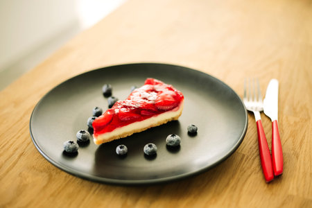Strawberry cheesecake with blueberries on black plate. Delicious food