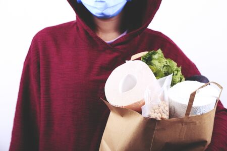Girl in protective mask is holding paper bag with food and toilet paper. Coronavirus outbreak. Panic.の写真素材