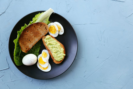 Healthy Breakfast with Toast and Boiled Eggs with Green Salad and Avocado on blue background