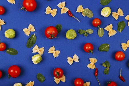 Colorful pizza ingredients pattern made of cherry tomatoes, basil and farfalle on blue background. Cooking concept.の写真素材