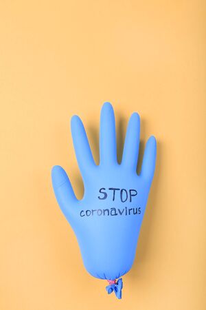 Protective blue rubber glove with STOP CORONAVIRUS text on yellow background. Coronavirus outbreakの写真素材