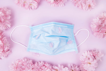 Medical protective mask and sakura flowers on a pink background. Medical protective mask in flowers....