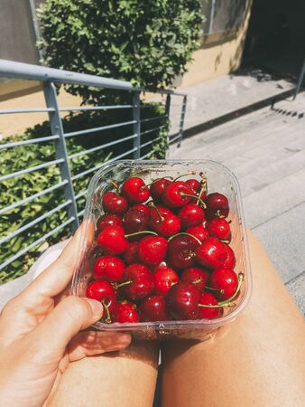 Girl's hand holding fresh cherries in plastic box outdoor. Healthy eatingの写真素材