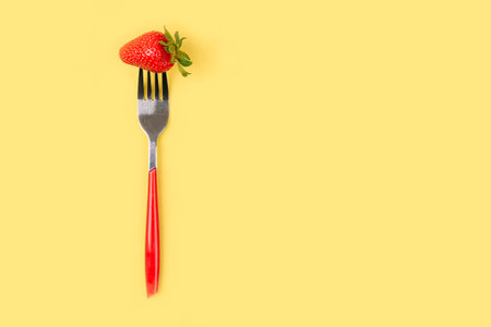 One strawberry on a red fork in the center of the yellow background. Top view. Vertical. Diet minimal concept.の写真素材