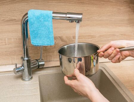 hands pour water into a pan for cooking in the kitchen in the houseの写真素材