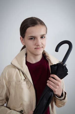 Stylish handsome teenager model holding a folded black umbrella on isolated grey backgroundの写真素材