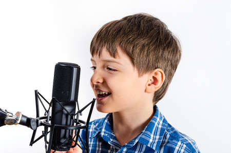 Kid in plaid shirt is singing in microphone close up isolated on white background. Boy having fun and play with microphone.の写真素材