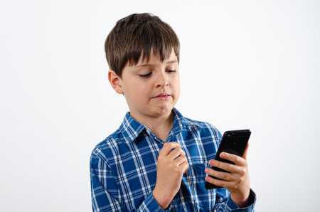 Portrait of a handsome boy is wearing plaid shirt with smartphone close up isolated on white background. Kid is carefully looking at the mobile phone.の写真素材