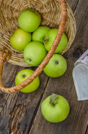 Ripe green apples in a wicker basket on an old rustic table. Summer harvest of aromatic apples. Useful fruits on wooden background.の写真素材