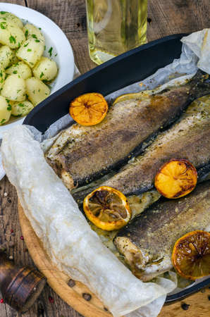 Baked whole rainbow trout with grilled lemon and boiled potatoes with herbs straight out of the oven. Cooked appetizing fish with potato garnish close-up. Healthy gourmet lunch.の写真素材