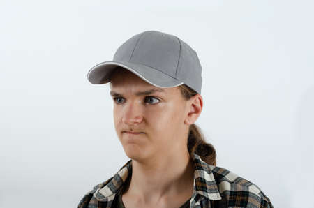 Fashion portrait of young man in grey baseball cap and checkered shirt with angry emotion on the white background. Studio portrait juvenile in casual clothes.の写真素材