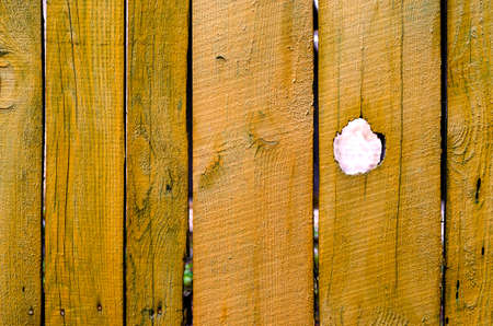 Old cracked yellow wooden fence with hole. Rough outdoor wooden texture.の写真素材
