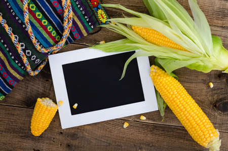 Cobs of ripe raw corn laid on dark wood textured table. White frame with black place for notes. Background, top view, close up, flat lay, copy space.の写真素材