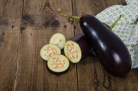 Two eggplants with slices on a rough wooden table. Vegetables for cooking.の写真素材
