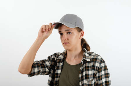 Trendy looking cool teenage boy adjusting baseball hat on his head, holding hands on peak on the white background. Studio portrait juvenile in casual clothes.の写真素材