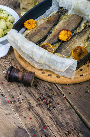 Baked whole rainbow trout with grilled lemon and boiled potatoes with herbs straight out of the oven. Cooked appetizing fish with potato garnish close-up. Healthy gourmet lunch.の写真素材