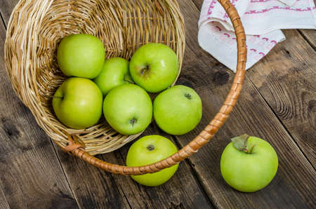 Ripe green apples in a wicker basket on an old rustic table. Summer harvest of aromatic apples. Useful fruits on wooden background.の写真素材