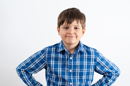 Portrait of a handsome boy is wearing plaid shirt with arms on hips on white background. Kid looking at the camera.の写真素材