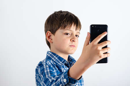 Portrait of a handsome boy is wearing plaid shirt with smartphone close up isolated on white background. Kid is carefully looking at the mobile phone.の写真素材