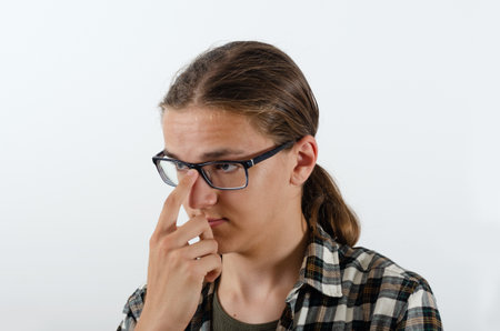 Smart teenager boy in a checkered shirt adjusts his glasses with finger and looks sideways on the white background, close-up. Studio portrait juvenile in casual clothesの写真素材