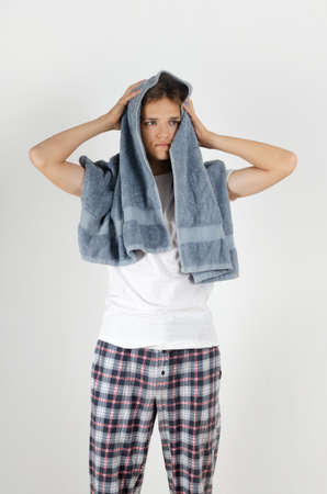 Cute caucasian teenager boy is drying hair with grey terry bath towel on white background. Young handsome man doing morning hygiene routine.の写真素材