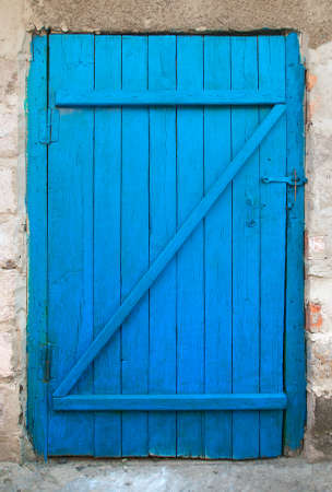 Closed old blue painted wooden door. Vintage entrance to a rural building closed with a homemade wooden door. Rough element of building.の写真素材