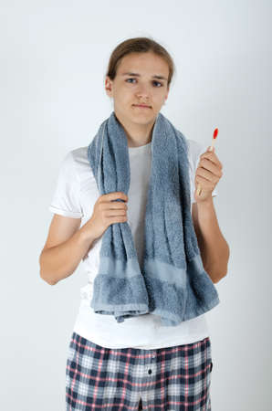 Handsome young man with terry grey bath towel over his neck is holding a toothbrush. Morning routine of washing the teeth.の写真素材