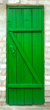 Closed old green painted wooden door. Vintage entrance to a rural building closed with a homemade wooden door. Rough element of building.の写真素材