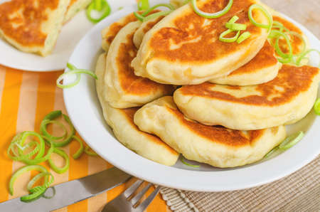 Delicious little fried pies on white plate with green onion. Appetizing pastries served for lunch. Traditional Russian pastry cuisine, homemade patties.の写真素材