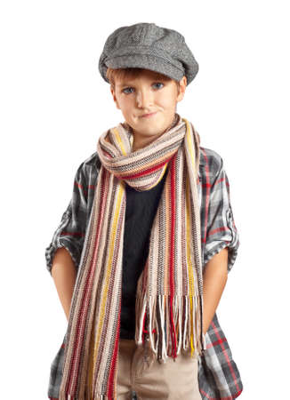 Cute grimacing boy posing with hands in the pockets on the white background. Boy is wearing in checkered shirt, beret and striped scarf looking front with ironic grimacing.の写真素材
