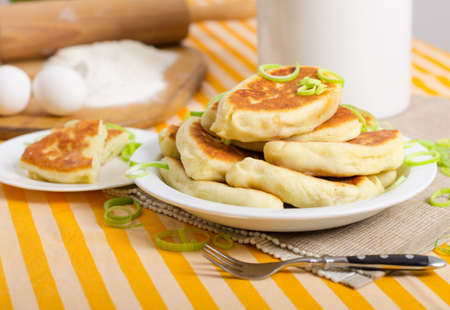 Delicious little fried pies on white plate with green onion. Appetizing pastries served for lunch. Traditional Russian pastry cuisine, homemade patties.の写真素材