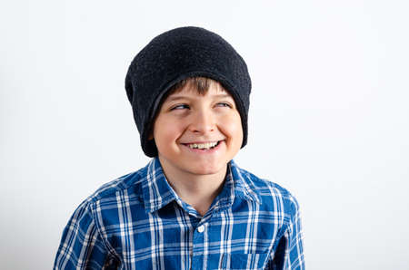 Portrait of a grimacing boy who wears plaid shirt and grey hat, isolated on white background. Kid with humor emotions looking with a squint.の写真素材