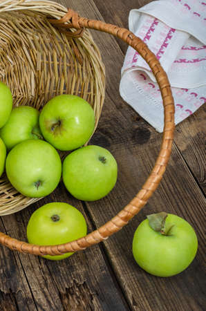 Ripe green apples in a wicker basket on an old rustic table. Summer harvest of aromatic apples. Useful fruits on wooden background.の写真素材