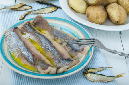 Salted herring fillet with oil on plate. Served dishes of marinated sliced fish and boiled potatoes on kitchen table. Traditional delicious food.の写真素材