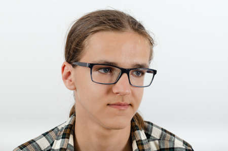Portrait of young man with glasses and checkered shirt with skeptical expression on the white background. Studio portrait juvenile in casual clothes.の写真素材