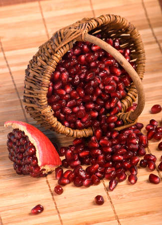 Basket with pomegranate seeds and piece of pomegranate with scattered seeds on on wood rug. Fresh tasty berries for eating. Useful vitamins for a healthy life.の写真素材