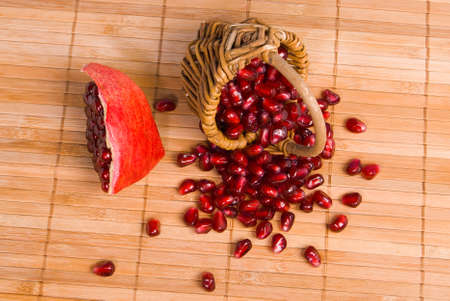 Small mini basket with pomegranate seeds and piece of pomegranate with scattered seeds on on woodden rug. Fresh tasty berries for eating. Useful vitamins for a healthy life.の写真素材