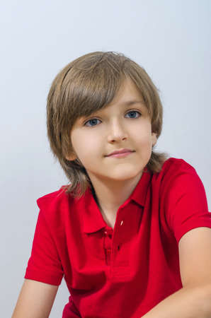 Portrait of cute kid sitting and looking away. A smart and neat child emotionally poses in a red t-shirt. Handsome and attractive boy at the studio shots.の写真素材