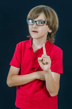 Teenager pointing a finger up and open mouth. Smart and tidy child on training in a red t-shirt. Quality childhood education for serious kids.の写真素材