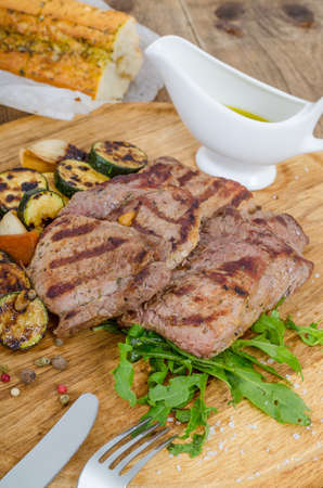 Grilled juicy barbecue steaks with fried marrow on a wooden round board. Prepared fresh food for breakfast, lunch or dinner. Lots of meat energy for good nutrition.の写真素材